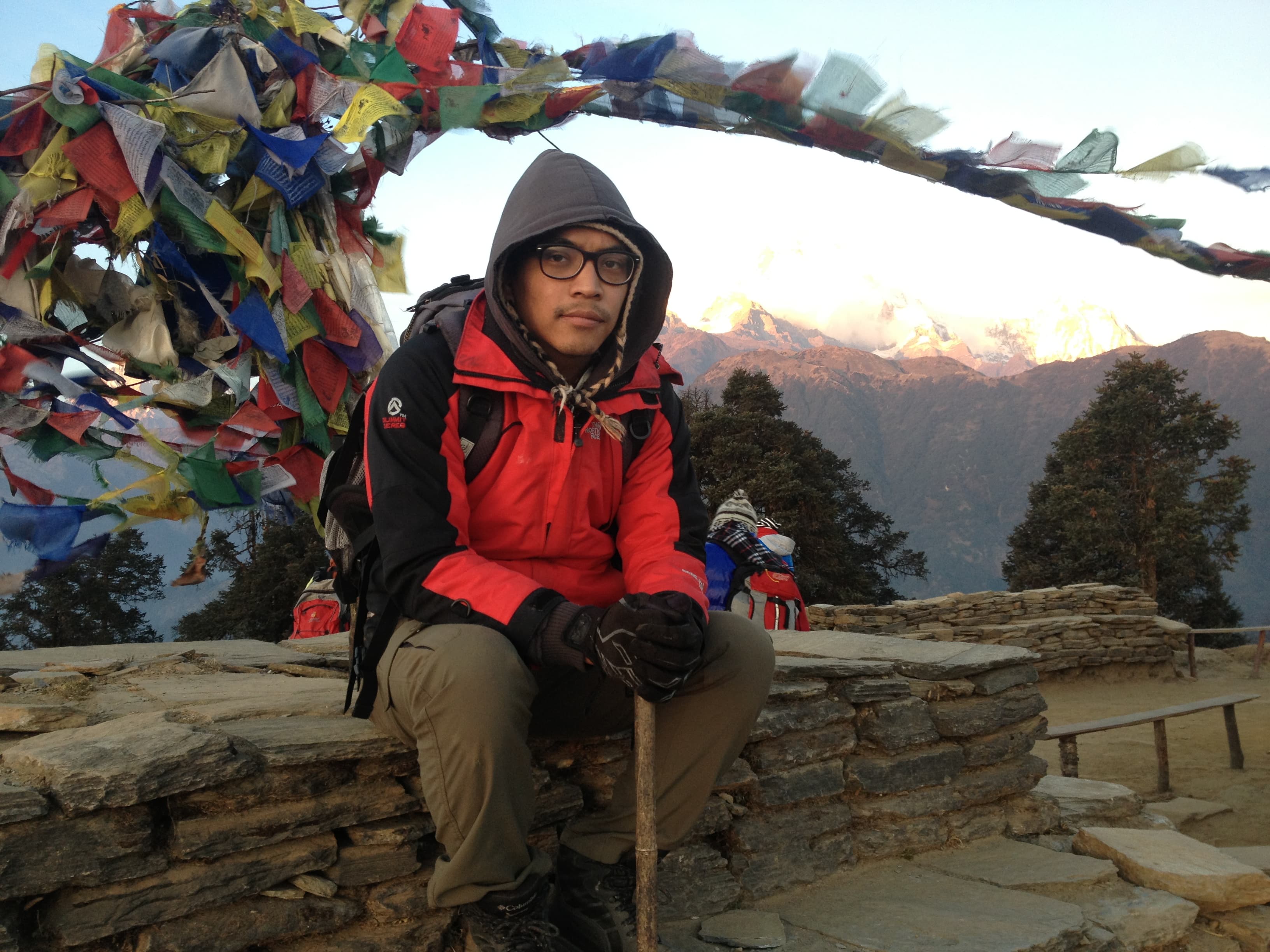 Milan sitting beneath colorful prayer flags with mountains behind him